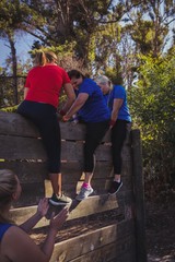 Woman being assisted to climb a wooden wall