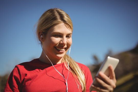 Fit woman listening music on mobile phone during obstacle course