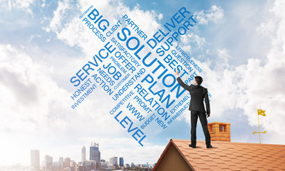 Young businessman standing on house roof and writing leadership skill concept. Mixed media