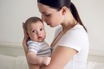 mother with her newborn son in hands sitting on a big white bed