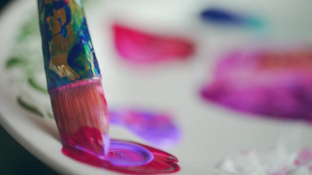 Close-up: painting with a brush and paints on a denim fabric. Brush with pink paint: the process of drawing. Details of the artist's work: drawing with a brush and paints. The artist draws on a denim.