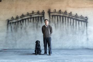A man and dog in front of a wall with a gate painting on it