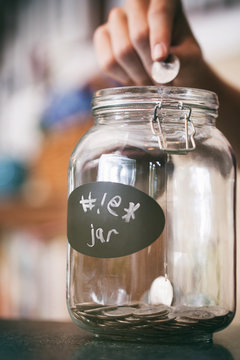 Close-up of a human hand inserting coin in saving jar