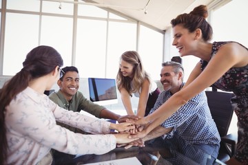 Happy business colleagues stacking hands on desk
