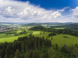 Aerial view of the summer time in mountains near Stronie Slaskie town in Poland. Pine tree forest and clouds over blue sky. View from above.