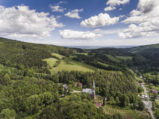 Fototapeta na wymiar Aerial view of the summer time in mountains in border Poland and Czech Republic. Pine tree forest and clouds over blue sky. View from above.