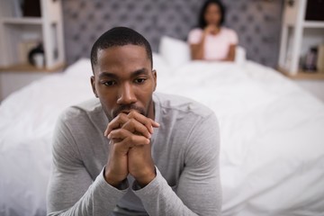 Man sitting while woman lying on bed at home