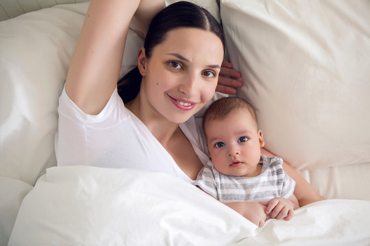 mom with a newborn son lying on a white bed