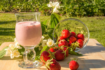 Sweet strawberry milkshake in the garden with strawberry on wood table and jasmine flower