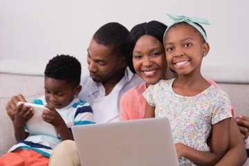 Happy family with laptop and digital tablet sitting on sofa