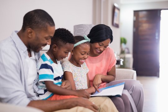 Smiling Family Reading Magazine While Sitting On Sofa