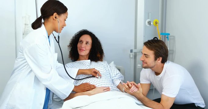 Doctor examining pregnant woman with stethoscope in ward