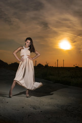 Fototapeta na wymiar Young girl at sunset wearing a long white dress