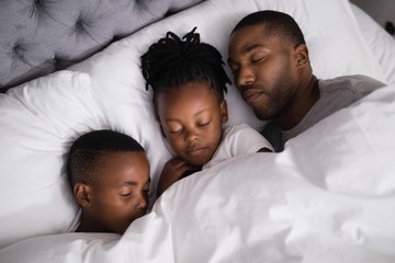 Father with children sleeping together on bed at home - Powered by Adobe
