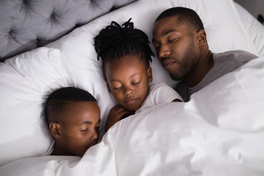 Father with children sleeping together on bed at home