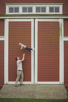 Dad throwing young son up in the air in front of farm barn door