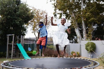 Playful siblings in costumes enjoying on trampoline