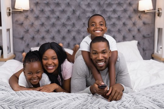 Portrait of happy family watching television while lying on bed