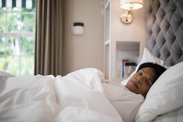 Mature woman sleeping on bed at home