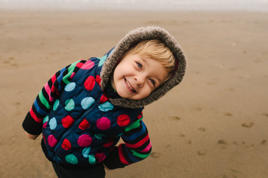 Happy, cheeky smiling girl in colourful winter clothes on a beach