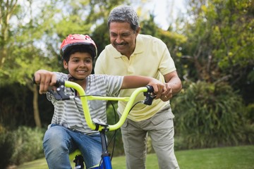 Obraz premium Grandfather assisting grandson while riding bicycle