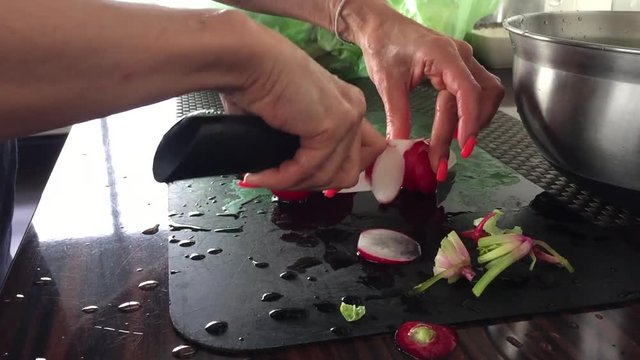 Female hands cutting radishes with ceramic knife 