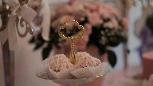 Close-up shot of cakes with cream capcake on festive table. Closeup shooting of Multi-tiered vase with cupcakes with pink protein custard standing on white tablecloth. On background unfocused flower