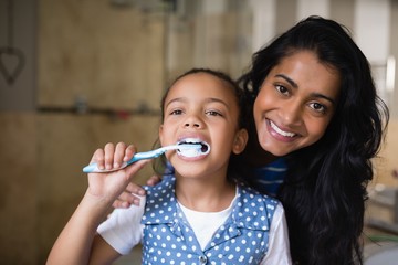 Girl brushing teeth with mother in bathroom