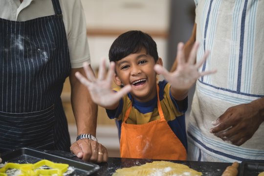 Portrait of happy boy showing messy hands while preparing food with father and grandfather in kitchen