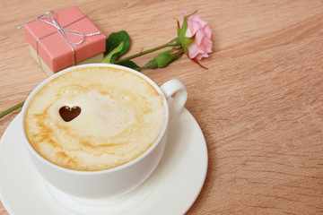 Coffee cappuccino in a white cup. A box with a gift and a rose.