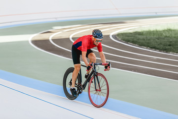 Racing cyclist on velodrome outdoor. Professional athlete in a red T-shirt and a black bicycle.