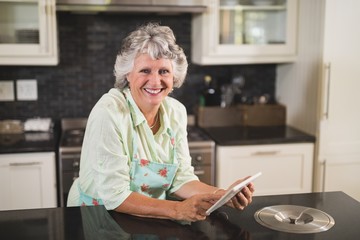 Fototapeta na wymiar Portrait of smiling senior woman using digital tablet on counter in kitchen at home