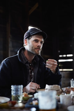 Man eating at a rustic picnic with friends inside a barn