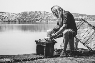 portrait of an old fishermen with long hair and white beard cutting a freshly caught fish