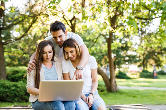 Amazig friends in nature sitting on bench and using laptop