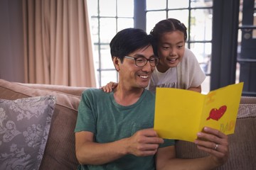 Father and daughter reading greeting card in living room