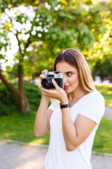 Cute girl on sunny day in park taking photos with analog camera