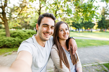 Obraz premium Cute and happy couple enjoying in park and taking selfie
