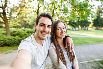 Obraz premium Cute and happy couple enjoying in park and taking selfie