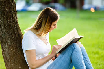 Young girl sitting in park and reading a book under the tree