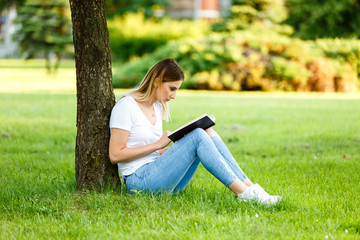 Beautiful girl sitting under the tree and reading her book