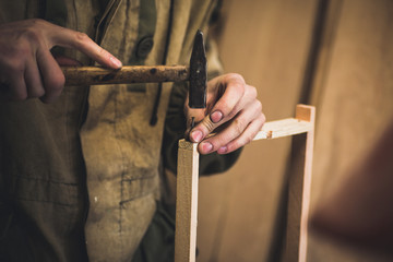 Man clogs a nail wooden frame for bees. Hands with long thin fingers hold wooden frame.