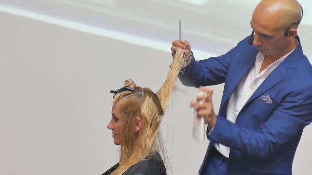 Stylist man cuts hair blonde Italian in a hairdressing salon