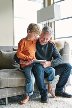 Father and son looking at digital tablet in on sofa in living room