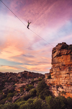 Man balance walking a highline or tight rope high over a rocky valley at sunset