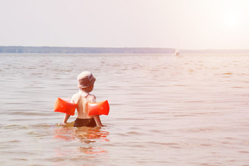 A small red-haired boy bathes on a hot summer day. Water splashes. A child spoils in the water. Leisure. Childhood
