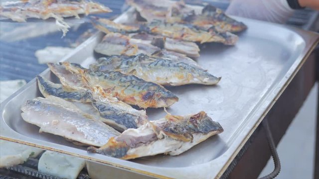 The cook lays grilled scomber fish on a tray. Outdoor summer barbecue