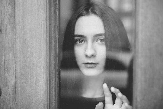 young woman standing at the window watching the street - Powered by Adobe