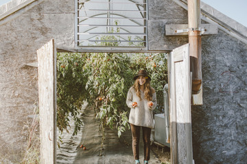 Bohemian girl stands outside of a greenhouse filled with tomatos