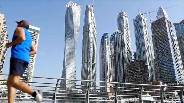 Low angle view of athletic fitness man running jogging in Dubai Marina in the morning, slow motion